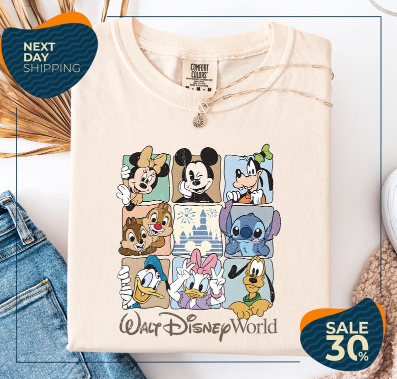 A white t-shirt with a graphic design of Disney characters, including Minnie Mouse, Mickey Mouse, Goofy, Donald Duck, and Pluto, arranged in a grid pattern. The t-shirt is displayed on a white background, and there are jeans visible in the background.