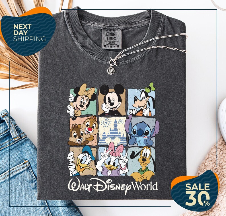 A gray t-shirt with a graphic of Disney characters, including Minnie Mouse, Mickey Mouse, Goofy, Donald Duck, and Pluto, arranged in a square pattern. The t-shirt is displayed on a white background, and there are jeans and a necklace visible in the image.