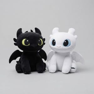 May include: Two plush dragon toys sitting side by side. The left dragon is black with large green eyes and small wings. The right dragon is white with large blue eyes and small wings. Both have rounded ears, smooth textures, and a seated posture.