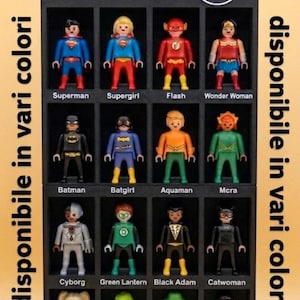 May include: A Playmobil display featuring DC Comics characters, including Superman, Batman, and Wonder Woman. The figures are in various colours and are displayed in individual compartments. The text "disponibile in vari colori" is visible.