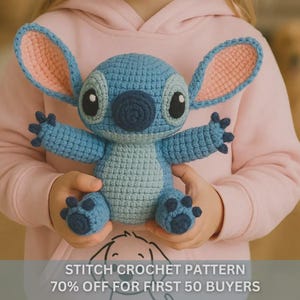 May include: A handmade blue crochet Stitch doll with large ears, black eyes, and a dark blue nose. The doll is held by a person wearing a pink hoodie. The image includes the text "STITCH CROCHET PATTERN".