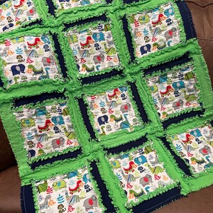 May include: A green and blue patchwork quilt with a dinosaur and elephant print. The quilt is made with a ruffled fabric and has a square pattern.