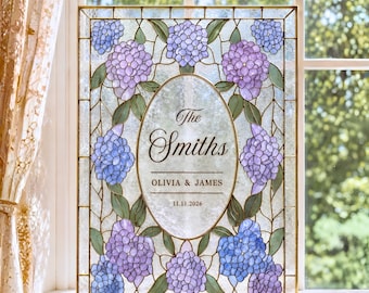 Può includere: Un pannello rettangolare in vetro colorato con un ovale centrale recante il testo The Smiths, OLIVIA & JAMES, e 11.11.2026. Il bordo è decorato con grappoli di fiori di ortensia blu e viola e foglie verdi, racchiuso in una cornice in metallo dorato.
