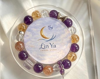 Op de afbeelding: Een kralenarmband met ronde paarse amethist, gele citrien en heldere kwartskralen, samen met een zilverkleurige metalen bedel. Een ronde kaart met een maansikkel-logo en de tekst Lin Ya CRYSTAL STUDIO is in het midden geplaatst.