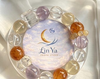 Op de afbeelding: Een kralenarmband met een mix van doorschijnende, bolvormige en kubusvormige kralen in tinten van transparant, lichtpaars, goudgeel en dieporanje. De armband omsluit een ronde kaart met een wolkenprint en de tekst Lin Ya Crystal Studio.