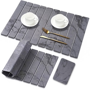 May include: A gray placemat set with a marble-like pattern, featuring two white teacups on saucers, gold-colored fork and knife, and a folded placemat. The set includes a coaster. The placemat is made of rectangular pieces.