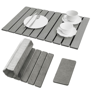 May include: Gray wooden placemats with a slatted design. One placemat has a white plate, fork, and knife. Another has two white teacups and saucers. Additional placemats and a coaster are also shown.