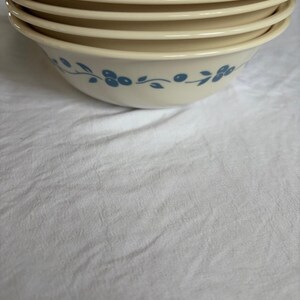 May include: A stack of cream-coloured ceramic bowls. Each bowl features a blue floral pattern around the rim. The bowls are stacked, with the top bowls in focus.