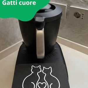 Könnte beinhalten: Schwarzes Küchengerät mit silbernem Griff und einer Basis mit weißer Umrandung von zwei Katzen, die sich ein Herz teilen. Der Text "Gatti cuore" befindet sich in einer grünen Blase.