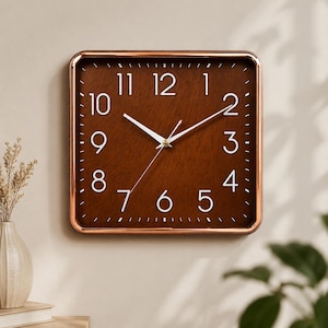 May include: A square wall clock featuring a dark brown wood-grain face with white Arabic numerals and thin white hands. The clock is encased in a polished metallic copper-toned frame, providing a clean and functional design for timekeeping.