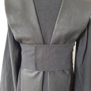 Puede incluir: T&uacute;nica negra con cuello de cuero y cintur&oacute;n de tela negro. La t&uacute;nica tiene un escote en V y mangas largas.
