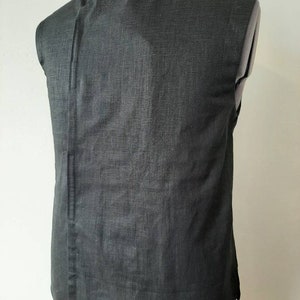 Puede incluir: Una camisa negra sin mangas con cuello mandar&iacute;n y un solo bot&oacute;n de cierre. La camisa est&aacute; hecha de una tela texturizada.