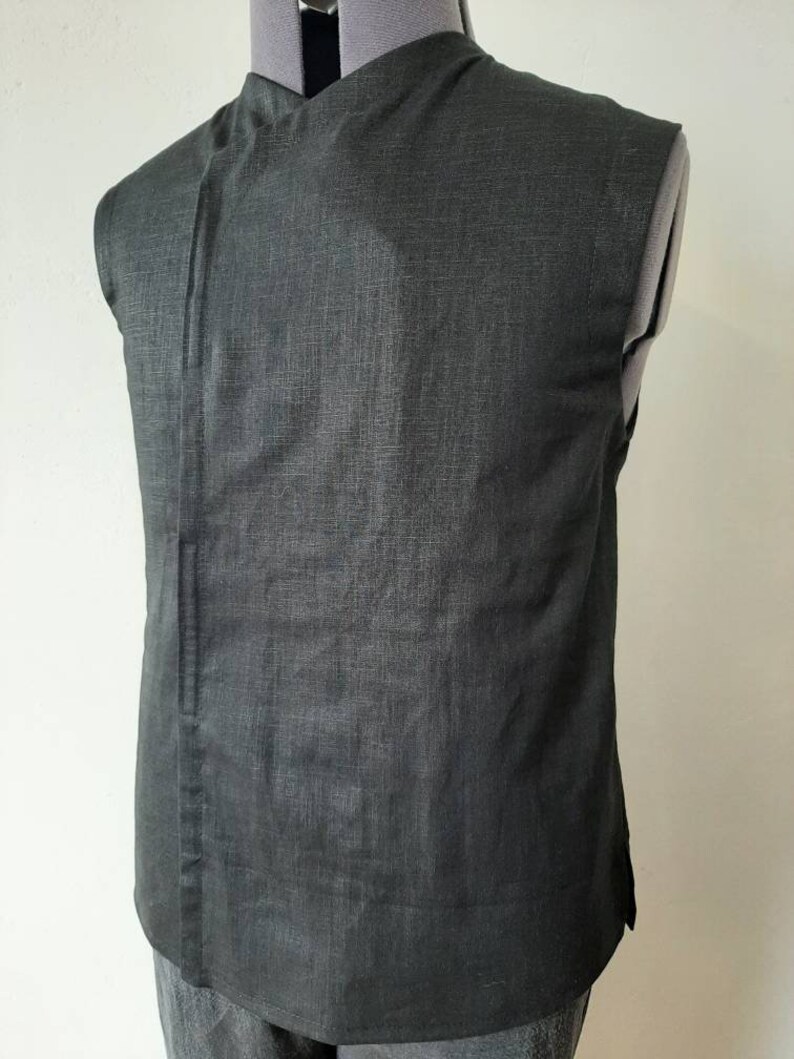 Puede incluir: Una camisa negra sin mangas con cuello mandar&iacute;n y un solo bot&oacute;n de cierre. La camisa est&aacute; hecha de una tela texturizada.