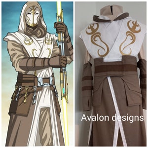 Op de afbeelding: Een wit en bruin Jedi-kostuum met een gouden riem en een lichtzwaard. Het kostuum heeft een capuchon met gouden borduurwerk en een masker. Het lichtzwaard is geel en heeft een groene kling. De tekst "Avalon designs" is zichtbaar in de rechterbenedenhoek van de afbeelding.
