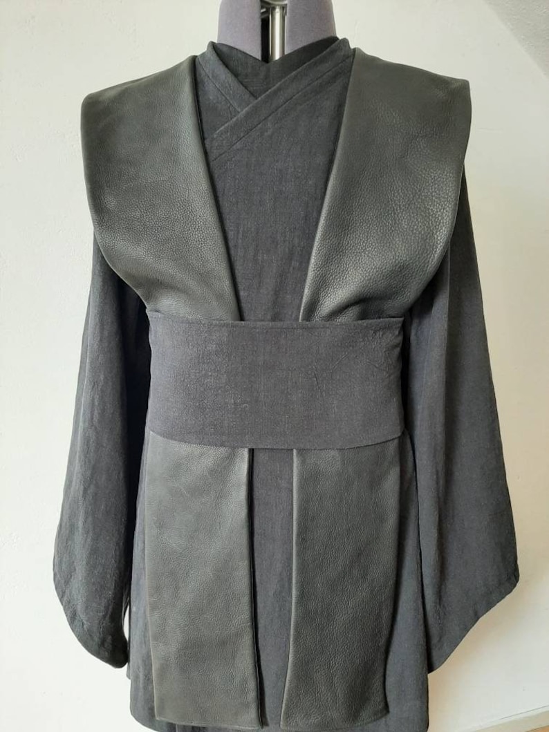Puede incluir: T&uacute;nica negra con cuello de cuero y cintur&oacute;n negro. La t&uacute;nica tiene un dise&ntilde;o largo y fluido y est&aacute; hecha de una tela suave y c&oacute;moda.