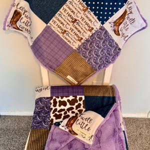May include: A patchwork baby blanket featuring squares of denim, brown corduroy, navy blue polka dots, purple paisley, and white fabric with cowboy boot illustrations and the text "sleep well little cowgirl" and "YE HAW". It has a soft purple backing.
