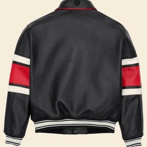May include: A black leather varsity jacket featuring a fold-down collar, long sleeves with horizontal red and white stripes, and a ribbed hem with black and white stripes. The jacket has a smooth finish and a button-down front closure at the bottom.