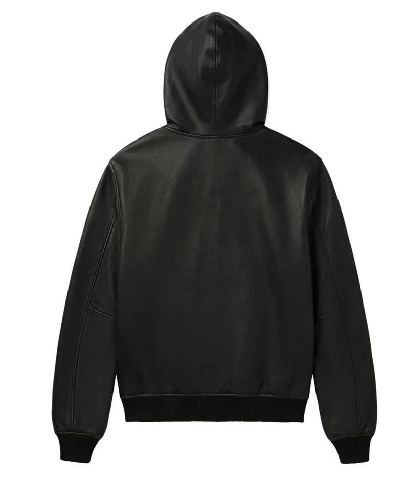 K&ouml;nnte beinhalten: Eine schwarze Lederjacke mit Kapuze, langen &Auml;rmeln sowie gerippten Strickb&uuml;ndchen an &Auml;rmeln und Saum. Die Jacke ist von der R&uuml;ckseite zu sehen und zeigt eine glatte, durchgehend schwarze Oberfl&auml;che &uuml;ber das gesamte Kleidungsst&uuml;ck hinweg.