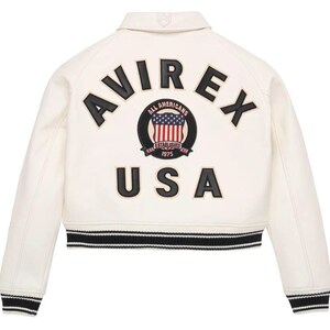 May include: An off-white varsity jacket featuring black lettering that reads AVIREX USA on the back. A circular patch in the center displays an American flag graphic with the text ALL AMERICANS ESTABLISHED 1975. The jacket has black and white striped ribbed trim.