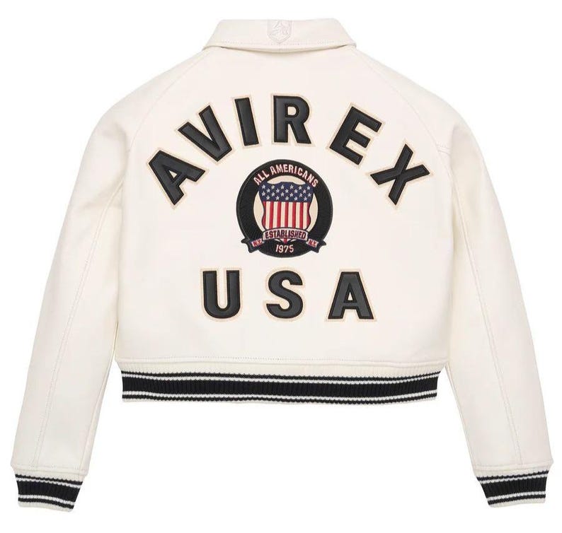 May include: An off-white varsity jacket featuring black lettering that reads AVIREX USA on the back. A circular patch in the center displays an American flag graphic with the text ALL AMERICANS ESTABLISHED 1975. The jacket has black and white striped ribbed trim.
