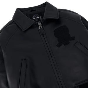 May include: A black leather jacket featuring a classic collar, a full-length front zipper with a branded pull, and two side pockets. An embroidered patch is visible on the chest, and the interior label displays the text AVIREX AUTHENTIC 1975.