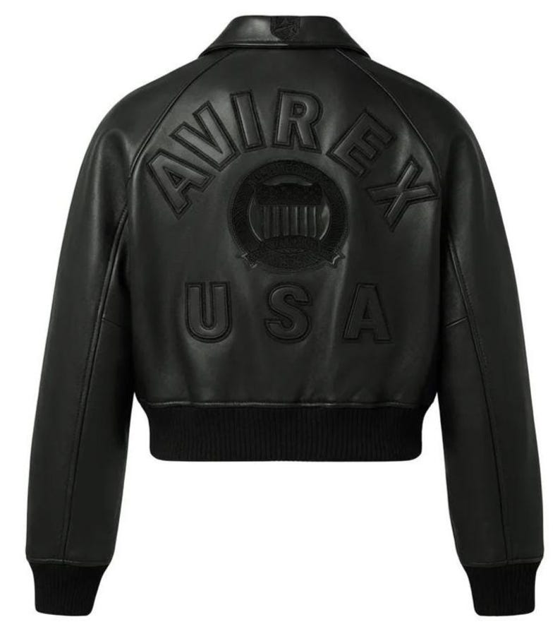 May include: A black leather bomber jacket featuring a ribbed collar, cuffs, and hem. The back displays embossed lettering that reads AVIREX USA, with a circular emblem positioned between the words, all rendered in a matching black tone.