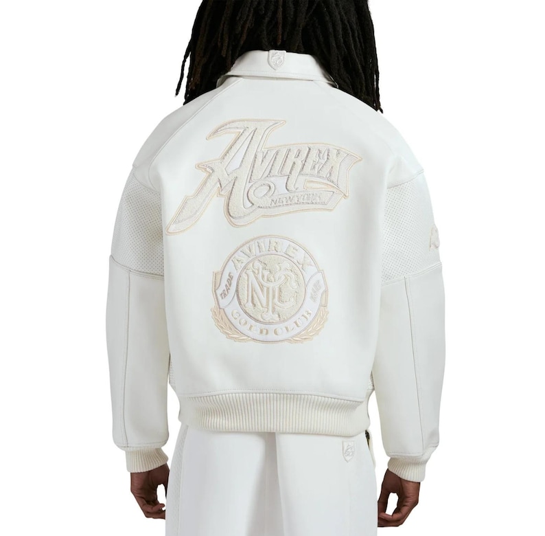 May include: An off-white varsity jacket featuring a large embroidered Avirex New York logo on the upper back and a circular Avirex Trade Mark NYC patch below it. The jacket has a ribbed collar, cuffs, and hem, with perforated leather sleeve panels.