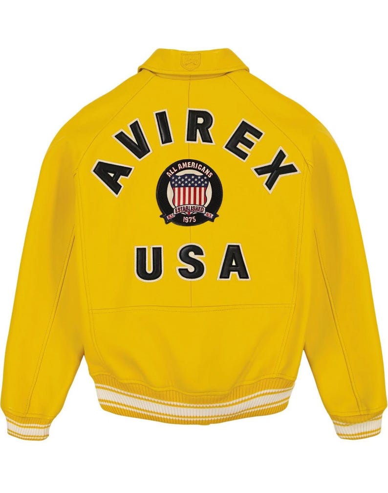 Pu&ograve; includere: Una giacca varsity giallo brillante con la scritta AVIREX in lettere nere arcuata sopra una toppa circolare con uno scudo a bandiera americana rosso, bianco e blu e il testo ALL AMERICANS ESTABLISHED 1975, con la scritta USA in nero sotto.