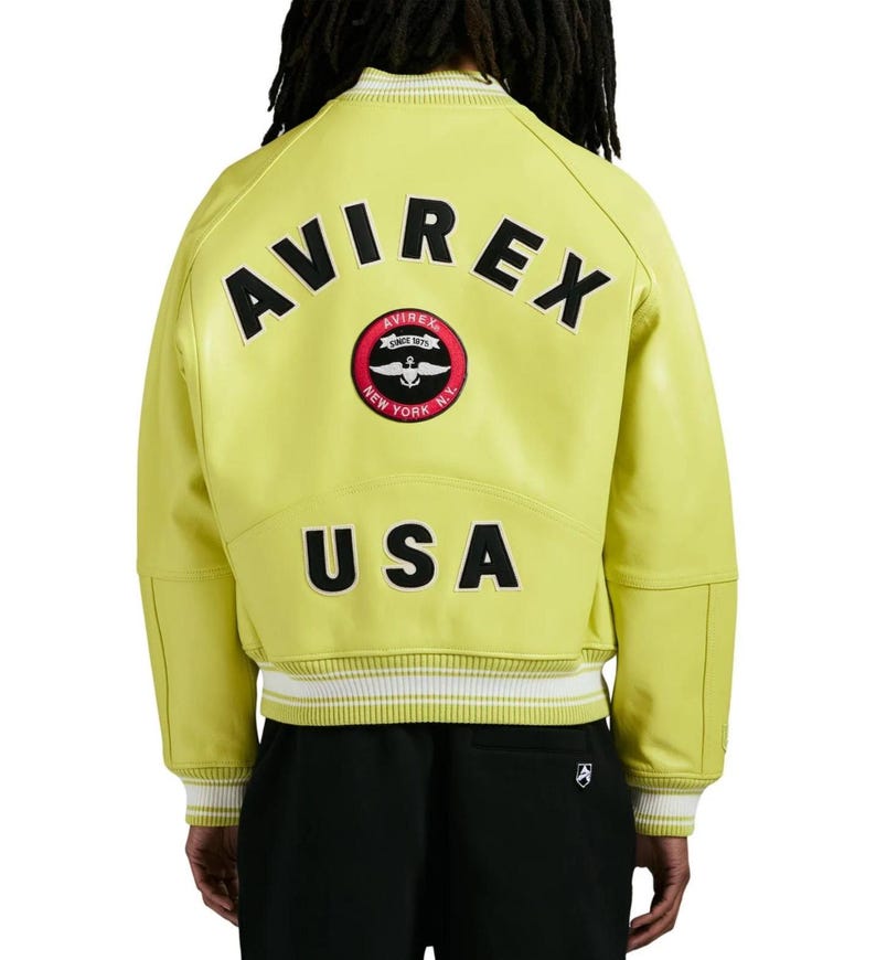 May include: A lime green varsity jacket featuring the text AVIREX in black letters across the upper back, a circular red and black patch with an anchor and wings logo, and the text USA in black letters above the white and lime green striped hem.