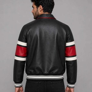 May include: A black leather jacket featuring a classic collar and long sleeves with prominent red and white horizontal stripes. The garment includes a ribbed hem and ribbed cuffs with white and black stripes, providing a structured fit.
