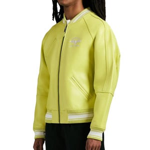 May include: A lime green bomber jacket featuring a front zipper closure, ribbed collar, and ribbed cuffs with white stripes. The jacket includes two slanted side pockets and a small embroidered emblem on the upper left chest area.