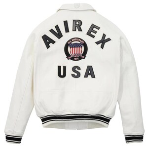 Puede incluir: Una chaqueta universitaria blanca con letras negras que dicen AVIREX y USA en la parte posterior. Un parche circular en el centro muestra una bandera estadounidense con el texto ALL AMERICANS ESTABLISHED 1975. La chaqueta tiene pu&ntilde;os acanalados a rayas.