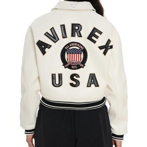 May include: An off-white varsity jacket featuring black lettering that reads AVIREX and USA on the back. A circular patch in the center displays a shield with the American flag, the text ALL AMERICANS, ESTABLISHED, and 1975. The jacket has striped trim.