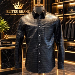 Può includere: Una camicia nera a maniche lunghe con una trama testurizzata in pelle di coccodrillo, dotata di colletto a punta, abbottonatura frontale con bottoni color argento e una singola tasca sul petto sul lato sinistro, esposta su un manichino.