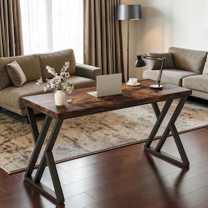 May include: A rectangular desk with a dark brown wood-grain surface and black metal legs arranged in a geometric X-shape. The desk features a flat top and a sturdy frame, providing a workspace for a laptop, a small white vase with flowers, and a lamp.