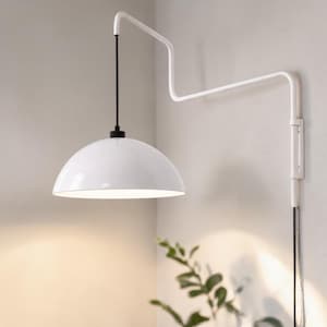 May include: A white, dome-shaped wall-mounted lamp with a black cord and a white, angular arm. The lamp is mounted on a light-colored wall, with a small plant in the corner. The lamp's design is minimalist and modern.