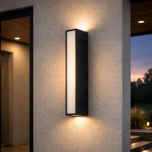 May include: A contemporary, rectangular outdoor wall light. The black fixture has a vertical, white light panel. It's mounted on a textured, light grey wall. The light emits a warm glow above and below the fixture, creating a welcoming ambiance.