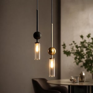 Op de afbeelding: Twee moderne hanglampen. Eén is zwart met een bolvormig accent en een heldere, geribbelde glazen kap. De andere is goudkleurig met een vergelijkbaar ontwerp. Beide geven een warm licht, ideaal voor een eetkamer of keuken.