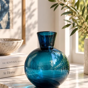 Op de afbeelding: Een ronde, diepblauwe glazen vaas met een glad, reflecterend oppervlak en een korte, uitlopende hals. De vaas heeft een bolvormig lichaam dat taps toeloopt naar een smalle opening, met een doorschijnende, levendige blauwe kleur in het glas.