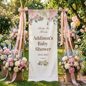 May include: A baby shower banner with the text "Baby In Bloom" and "Addison's Baby Shower 09.15.2027". The banner is decorated with floral designs and is flanked by baskets of flowers and pink ribbons. The scene is set outdoors.
