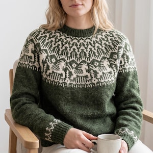 May include: A green and cream-colored sweater with a crew neck. The sweater features a geometric pattern across the chest and upper sleeves. The lower portion of the sweater is a solid green color. The sleeves have a matching pattern at the cuffs.