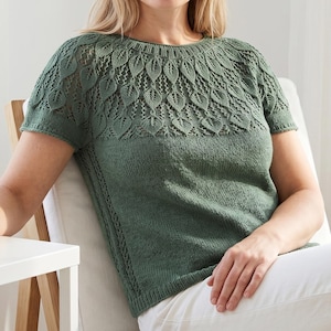 May include: A green short-sleeved knit top with a leaf-patterned yoke. The top has a round neckline and is made of a soft, textured yarn. The model is wearing white pants. The top is a comfortable and stylish garment.