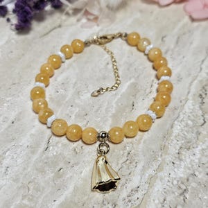 Könnte beinhalten: Ein Armband aus runden, durchscheinenden gelben Edelsteinperlen, die mit kleinen weißen Zwischenperlen abwechseln. Das Armband verfügt über einen goldfarbenen Metallanhänger in Geisterform an einer Mittelperle und einen Karabinerverschluss.