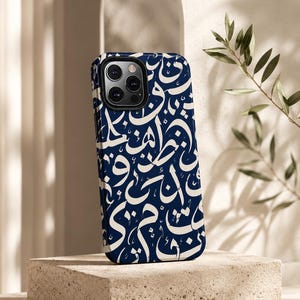 Peut inclure: Une coque de smartphone bleu foncé ornée d'un motif de calligraphie arabe blanche sur toute la surface. La coque présente une découpe rectangulaire pour le bloc optique dans le coin supérieur gauche, révélant trois objectifs et un flash.