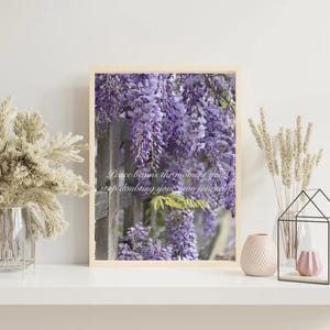 Op de afbeelding: Een rechthoekige wandkunstprint met een tros paarse blauweregenbloemen die over een houten hek hangen. De tekst "Peace begins the moment you stop doubting your own journey" is in witte schrijfletters in het midden afgedrukt.
