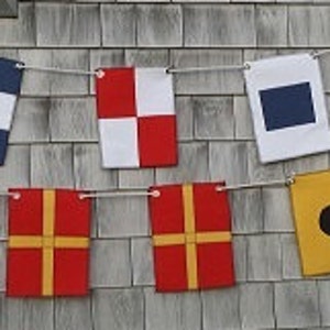 May include: A string of nautical signal flags in various colors, including red, white, blue, and yellow, strung across a gray shingled wall. The phrase "JUST MARRIED" is written in black text at the bottom.