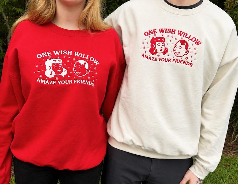 Puede incluir: Una sudadera roja y una sudadera color crema, ambas con un estampado gr&aacute;fico de dos caras de dibujos animados y el texto "ONE WISH WILLOW AMAZE YOUR FRIENDS". La sudadera roja tiene texto blanco y la sudadera color crema tiene texto rojo.