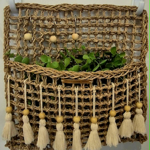 May include: A rectangular woven seagrass wall pocket organiser featuring a grid pattern, three metal hooks with wooden beads, and a row of nine off-white cotton tassels with wooden beads along the bottom edge. A small wooden tag reads Wandering Muse.