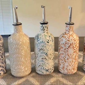 Può includere: Cinque bottiglie decorative in ceramica con beccucci in acciaio inossidabile. Le bottiglie presentano motivi floreali in vari colori, tra cui blu, crema, verde, arancione e un design multicolore. Adatto per olio o aceto.