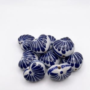 May include: A collection of small, heart-shaped ceramic beads featuring a glossy white finish with hand-painted deep blue radial patterns. Each bead has a central hole for stringing, showcasing a smooth, rounded surface and a consistent design.